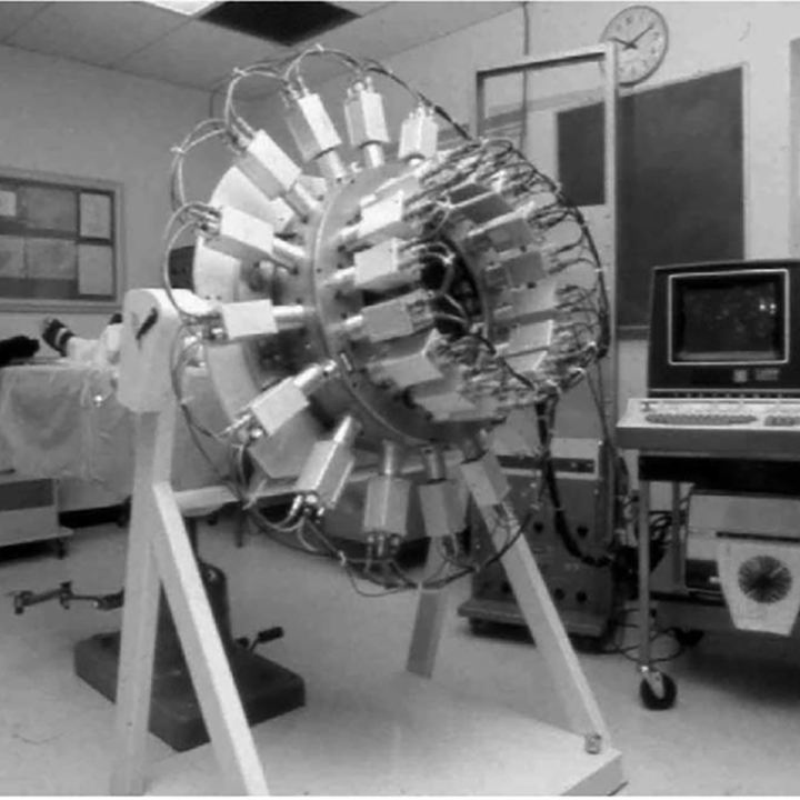 In the centre of a
university lab room stands a large mechanical device with protruding parts
that form a circle. To the right is a monitor on a cart with wheels.