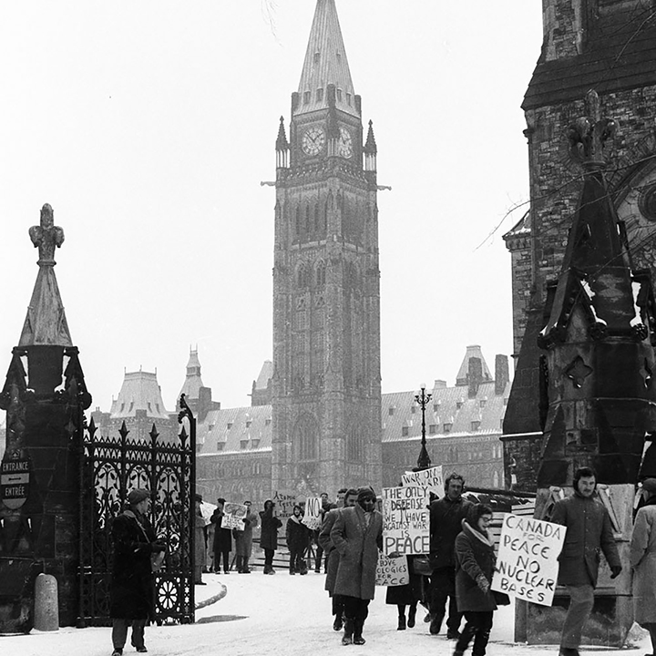 Une foule détudiants franchit la clôture ouverte sur la Colline du
Parlement, à Ottawa. La tour de la Paix figure en arrière-plan. Plusieurs
étudiants tiennent des affiches demandant la paix.
