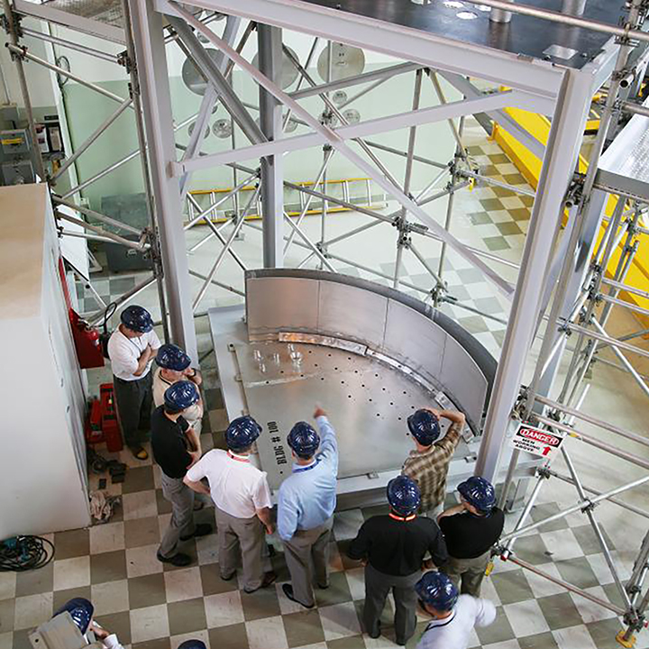 Vue du haut dun
plancher en damier, où 11 personnes vêtues de casques de sécurité
observent le réacteur NRU réparé. 