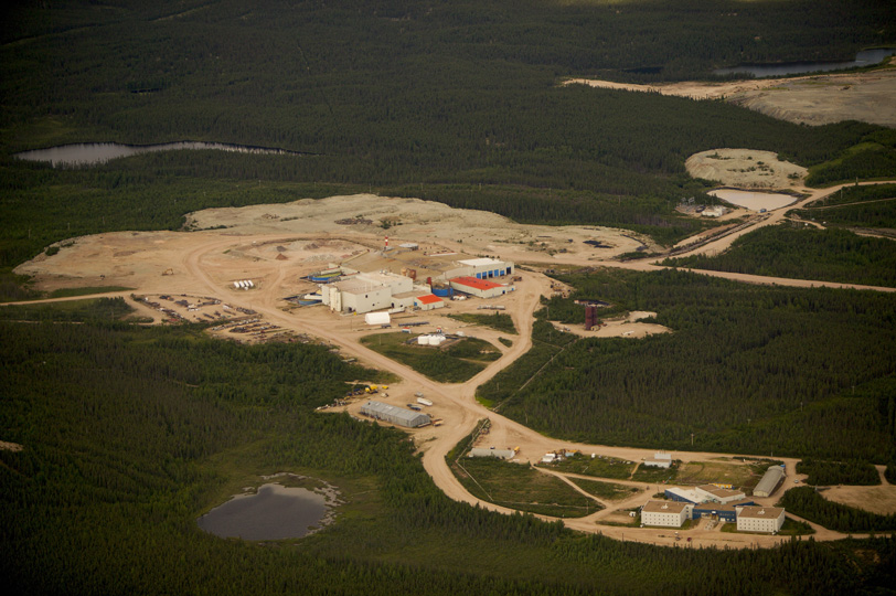 A sandy beige clearing in the centre of a green, wooded forest area extends out with various paths that connect to other clearings. There are squared white, blue and red buildings on the sand. Within the wooded area are 3 small gray bodies of water.