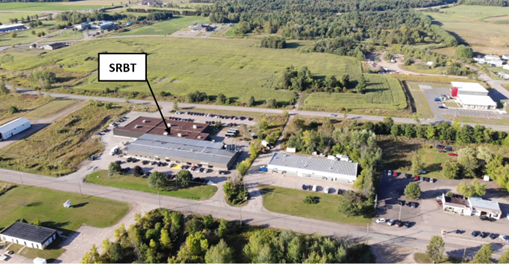 The SRBT facility is shown in an aerial photo. Its location is in a strip mall, surrounded by small roads and fields.