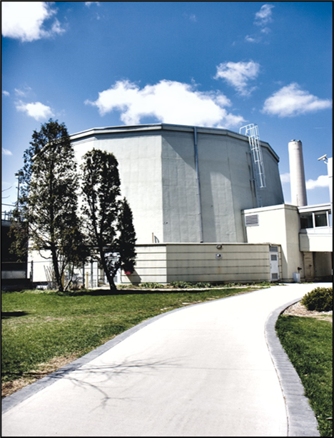 The building is located next to a path, surrounded by a lawn. Two trees stand next to the building. 