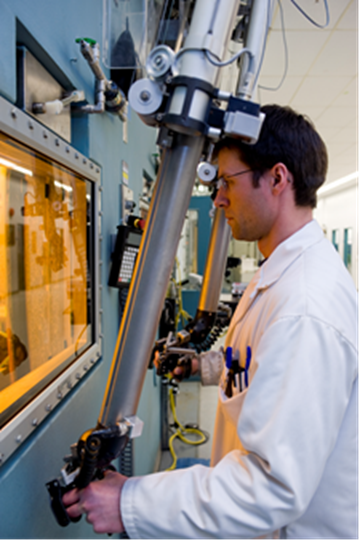 Cette photo montre un employé de Nordion qui regarde dans une cellule chaude en utilisant un manipulateur pour contrôler le bras robotisé.