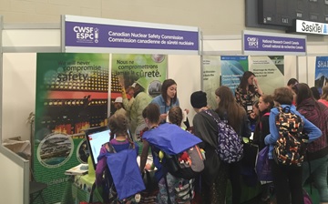 A CNSC employee engages with several students at the CNSC booth, displaying content on a computer screen at the 2018 Canada-Wide Science Fair.