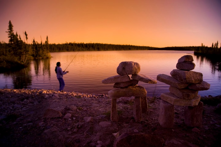 A man fishing in a lake with inukshuks on the shore